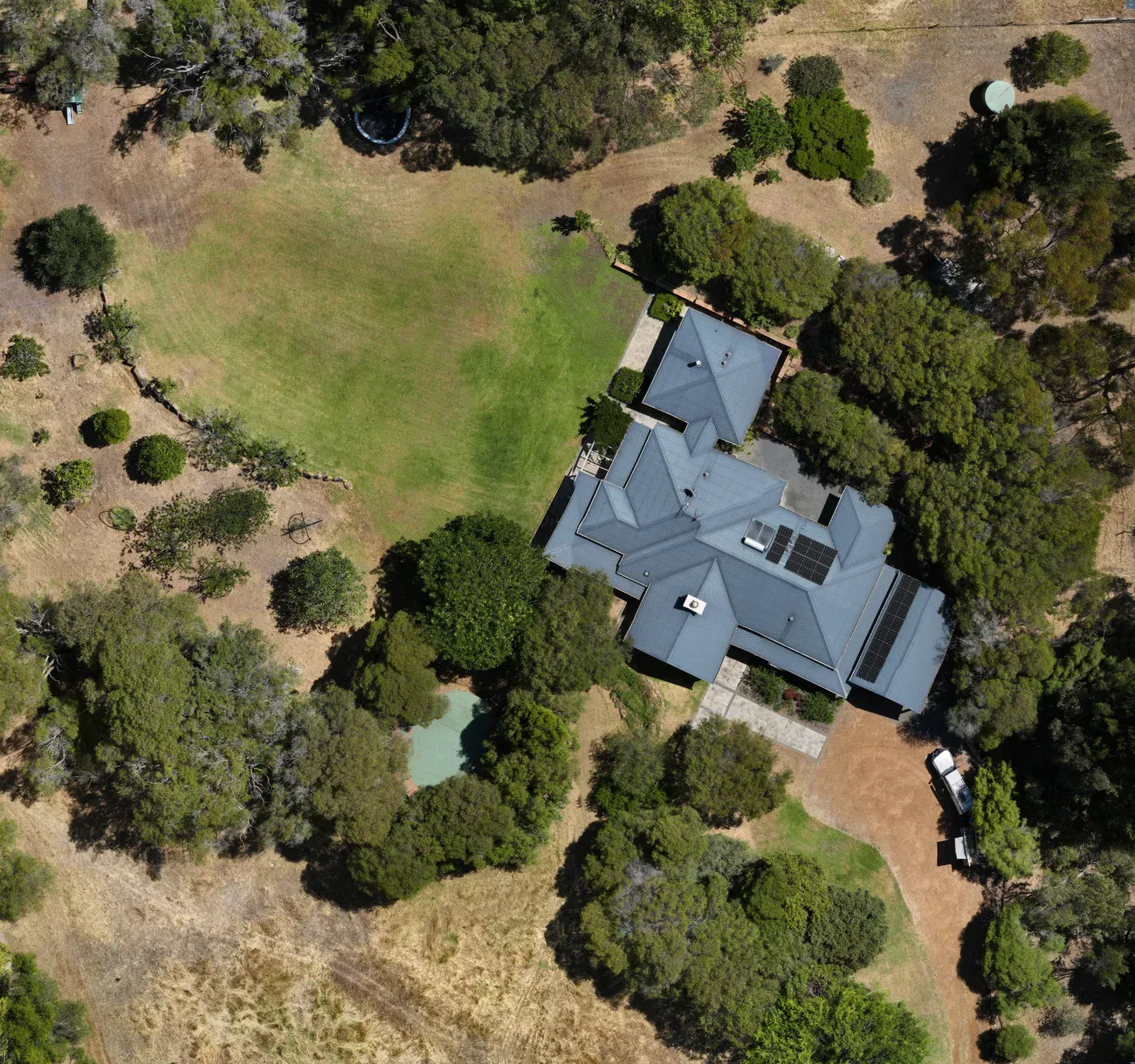 High-resolution aerial photograph of a rural property — homestead with grey roof, lawn, dam and established trees, sharp enough for print